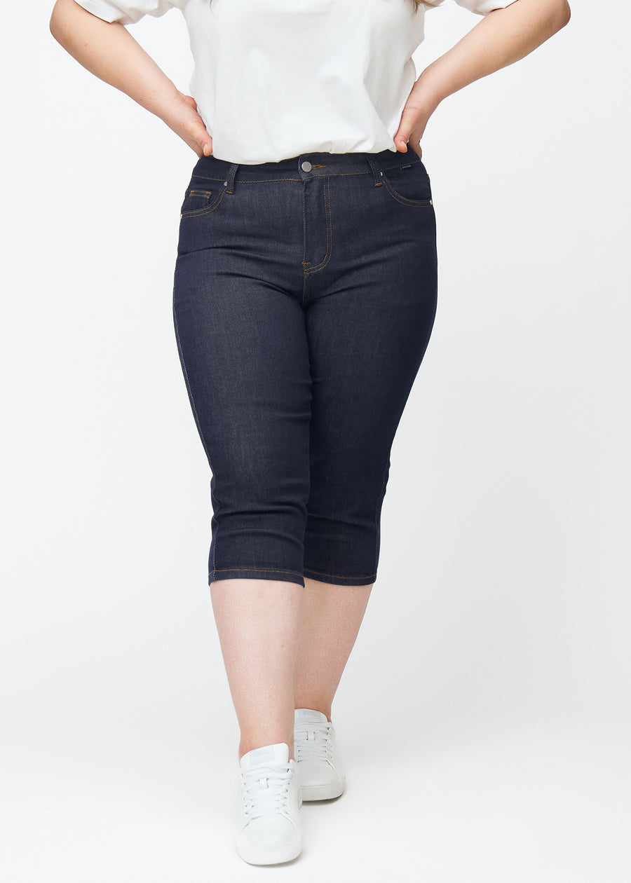 Dyp mørkeblå denim capris til dame i fargen Midnights med skinny passform sett forfra på plus-size modell.