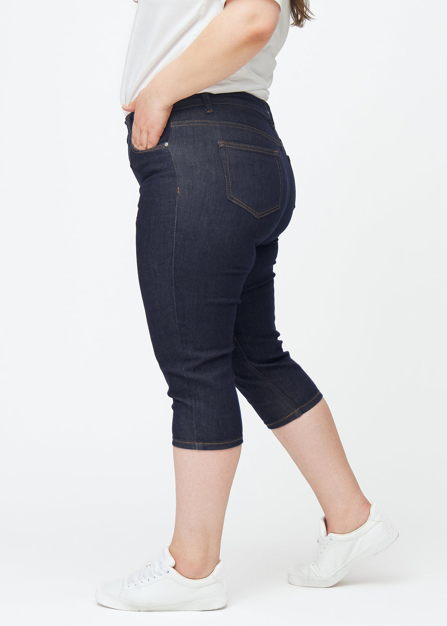 Dyp mørkeblå denim capris til dame i fargen Midnights med skinny passform sett fra siden på plus-size modell.