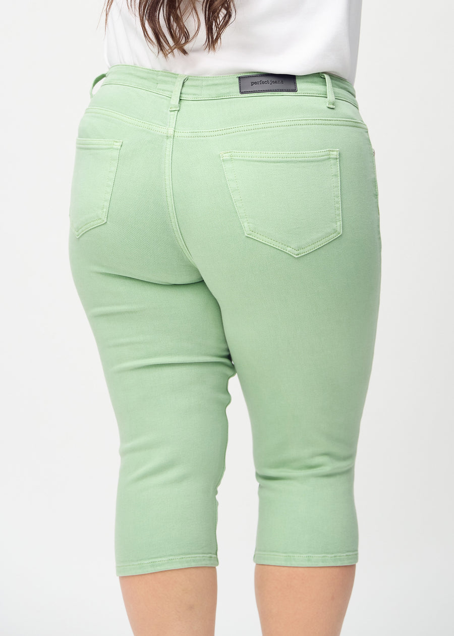 Skinny-capris til kvinner i pastellgrønt jeansstoff, fargen Mints. Nærbilde bakfra på en plus size-modell, med fokus på lommer og sømmer.