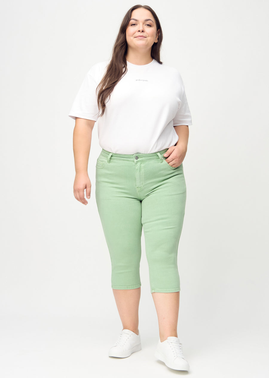 Skinny-capris til kvinner i pastellgrønt jeansstoff, fargen Mints. Helhetsbilde av en plus size-modell med capris på.