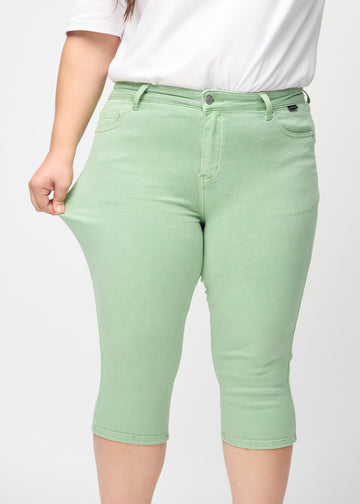 Skinny-capris til kvinner i pastellgrønt jeansstoff, fargen Mints. En plus size-modell strekker stoffet for å vise fleksibiliteten.