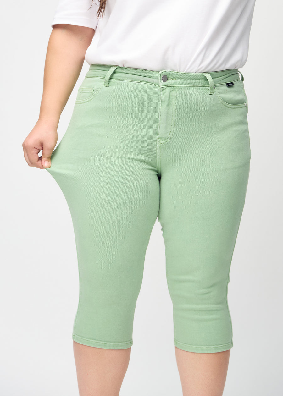 Skinny-capris til kvinner i pastellgrønt jeansstoff, fargen Mints. En plus size-modell strekker stoffet for å vise fleksibiliteten.