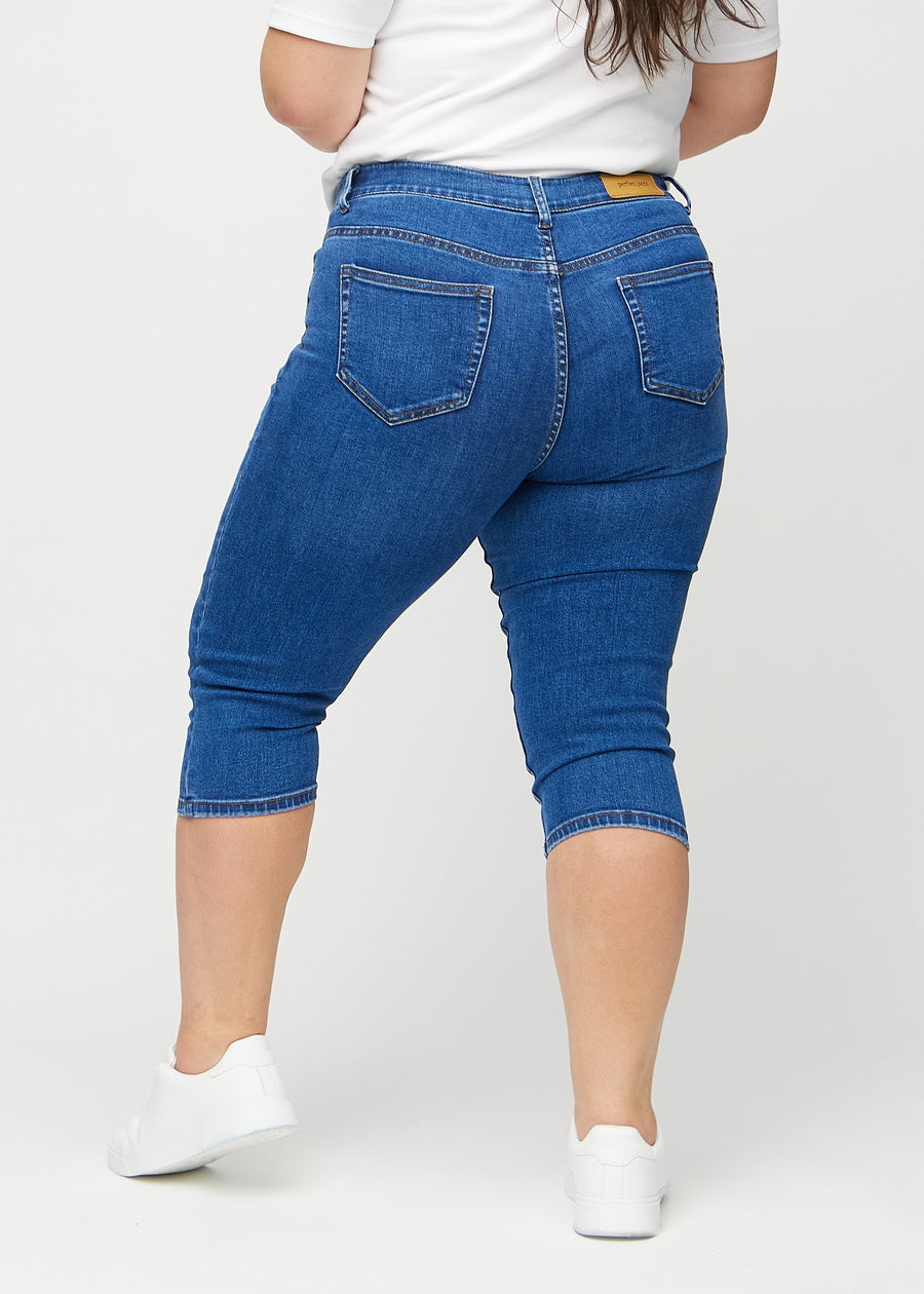 Skinny-capris til kvinner i mørkeblå denim, fargen Oceans. Sett bakfra på en plus size-modell, med fokus på passform og baklommer.