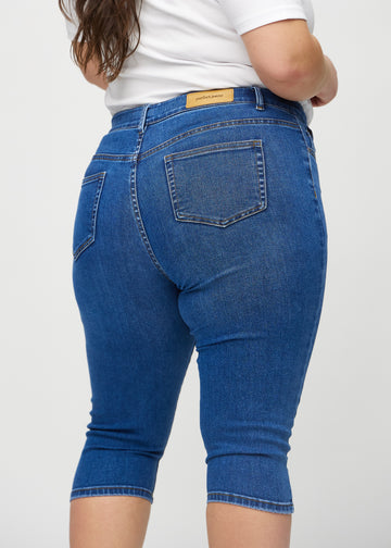 Skinny-capris til kvinner i mørkeblå denim, fargen Oceans. Nærbilde bakfra på en plus size-modell, med fokus på lommer og sømmer.