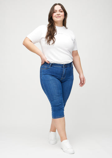 Skinny-capris til kvinner i mørkeblå denim, fargen Oceans. Helhetsbilde av en plus size-modell med capris på.