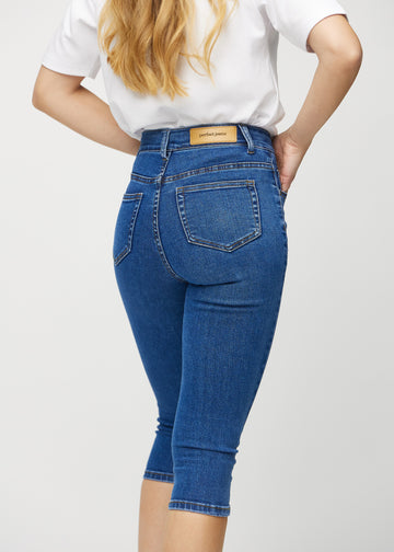 Skinny-capris til kvinner i mørkeblå denim, fargen Oceans. Nærbilde bakfra på en modell, med fokus på lommer og sømmer.