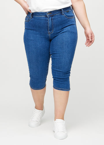 Skinny-capris til kvinner i mørkeblå denim, fargen Oceans. Sett forfra på en plus size-modell, med tettsittende ben til rett under kneet.