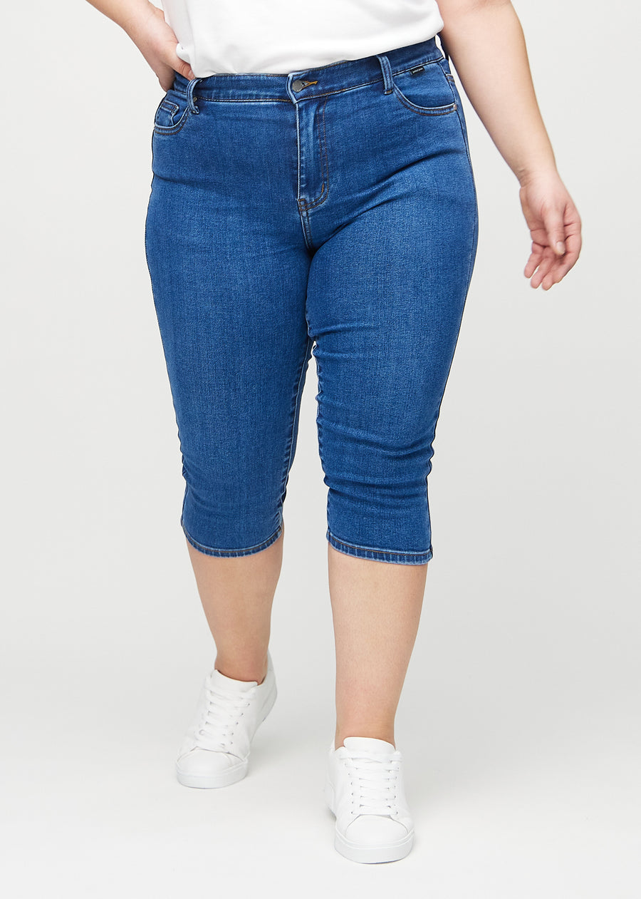 Skinny-capris til kvinner i mørkeblå denim, fargen Oceans. Sett forfra på en plus size-modell, med tettsittende ben til rett under kneet.