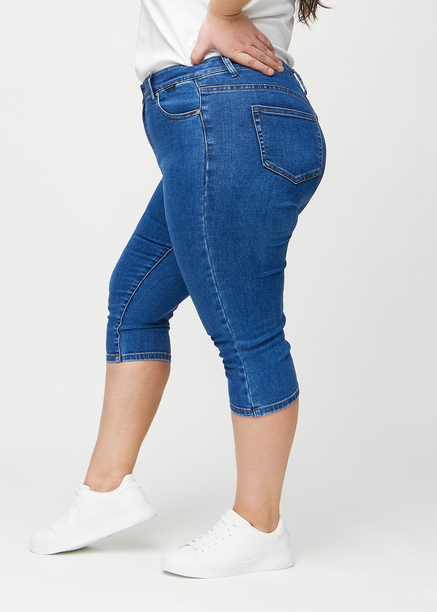 Skinny-capris til kvinner i mørkeblå denim, fargen Oceans. Sett fra siden på en plus size-modell, med tettsittende passform.