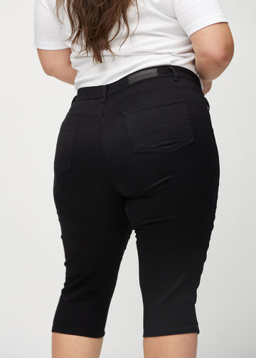 Svarte skinny capris sett bakfra på nært hold på en plus-size-modell for å vise detaljer.