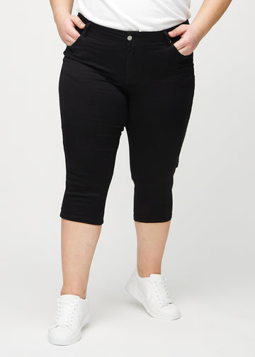 Svarte skinny capris, modellnavn Ravens, som sitter tett til benet og slutter rett under kneet på en plus-size-modell, sett forfra.