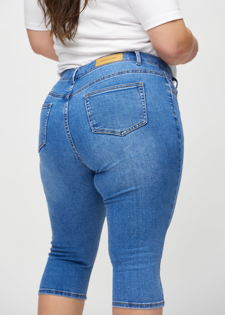 Skinny-capris til kvinner i blå denim, fargen Rivers. Nærbilde bakfra på en plus size-modell, med fokus på lommer og sømmer.