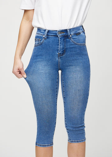 Skinny-capris til kvinner i blå denim, fargen Rivers. En modell strekker stoffet for å vise fleksibiliteten.