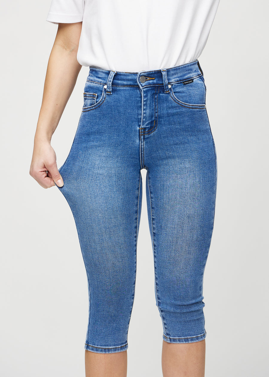 Skinny-capris til kvinner i blå denim, fargen Rivers. En modell strekker stoffet for å vise fleksibiliteten.