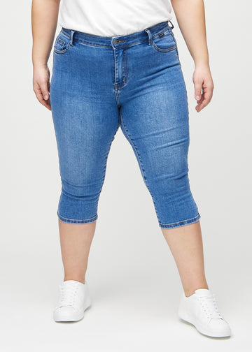 Skinny-capris til kvinner i blå denim, fargen Rivers. Sett forfra på en plus size-modell, med tettsittende ben til rett under kneet.