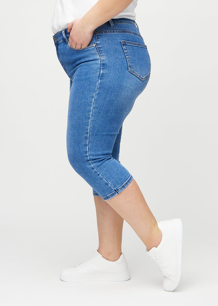 Skinny-capris til kvinner i blå denim, fargen Rivers. Sett fra siden på en plus size-modell, med tettsittende passform.