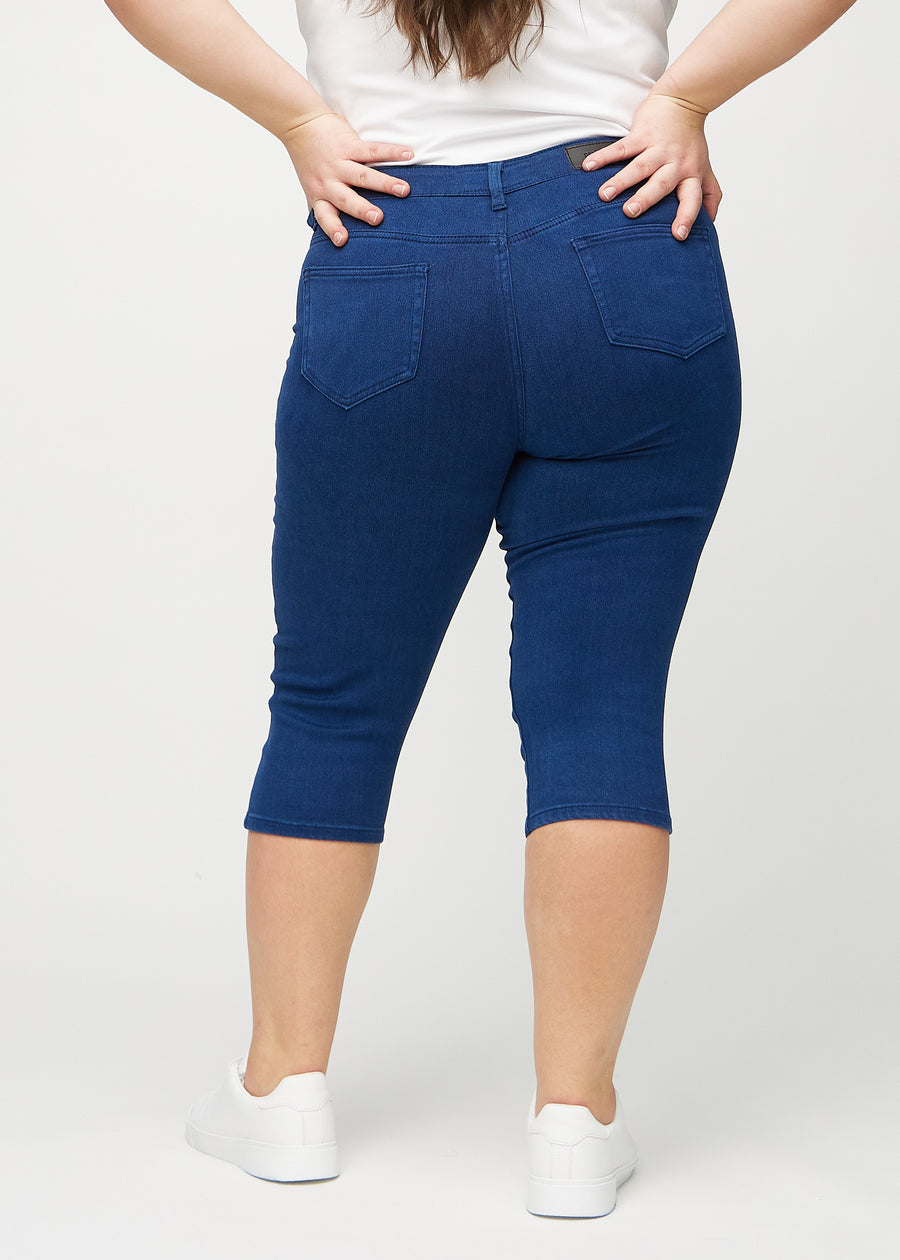 Skinny-capris til kvinner i mørkeblått jeansstoff, fargen Royals. Sett bakfra på en plus size-modell, med fokus på passform og baklommer.