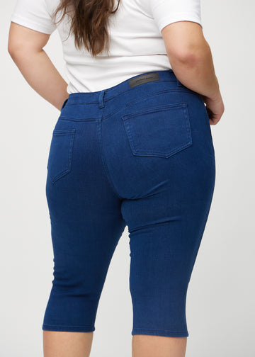 Skinny-capris til kvinner i mørkeblått jeansstoff, fargen Royals. Nærbilde bakfra på en plus size-modell, med fokus på lommer og sømmer.