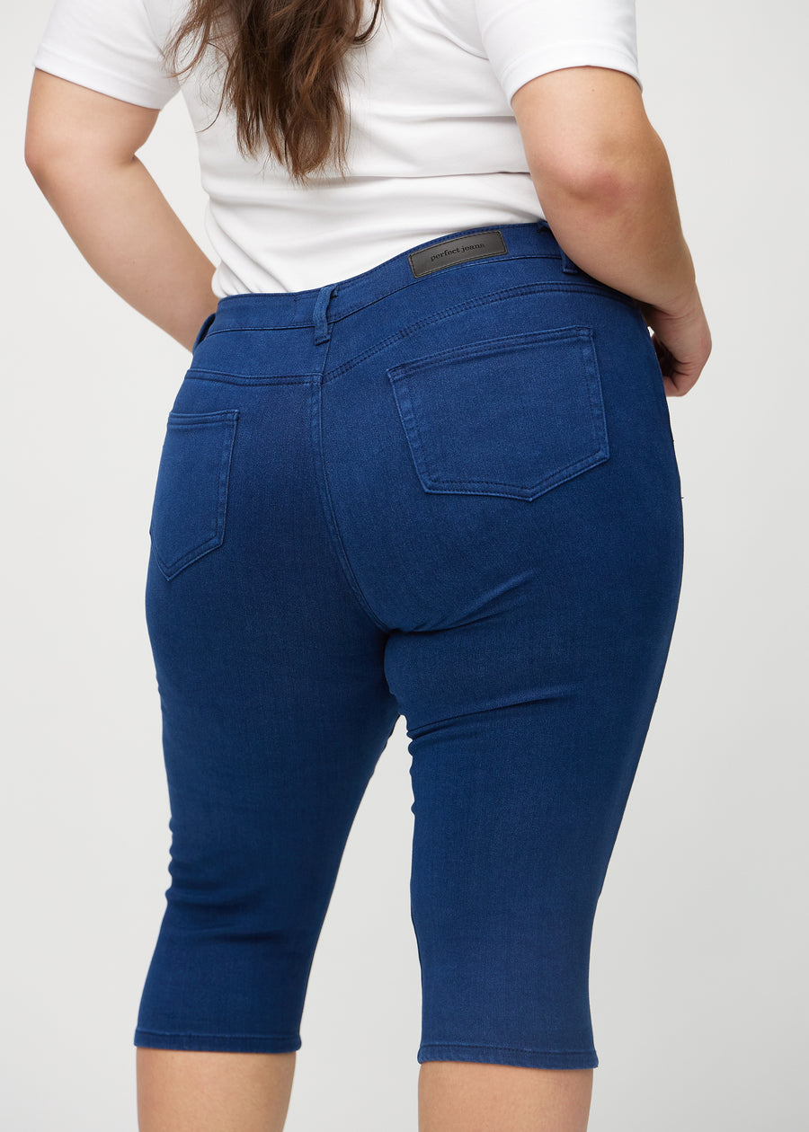 Skinny-capris til kvinner i mørkeblått jeansstoff, fargen Royals. Nærbilde bakfra på en plus size-modell, med fokus på lommer og sømmer.