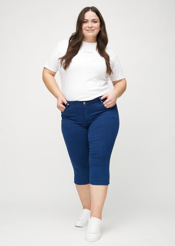Skinny-capris til kvinner i mørkeblått jeansstoff, fargen Royals. Helhetsbilde av en plus size-modell med capris på.