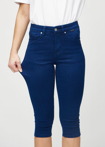 Skinny-capris til kvinner i mørkeblått jeansstoff, fargen Royals. En modell strekker stoffet for å vise fleksibiliteten.