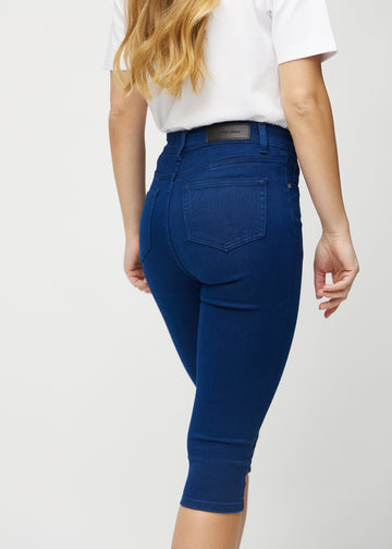 Skinny-capris til kvinner i mørkeblått jeansstoff, fargen Royals. Nærbilde bakfra på en modell, med fokus på lommer og sømmer.