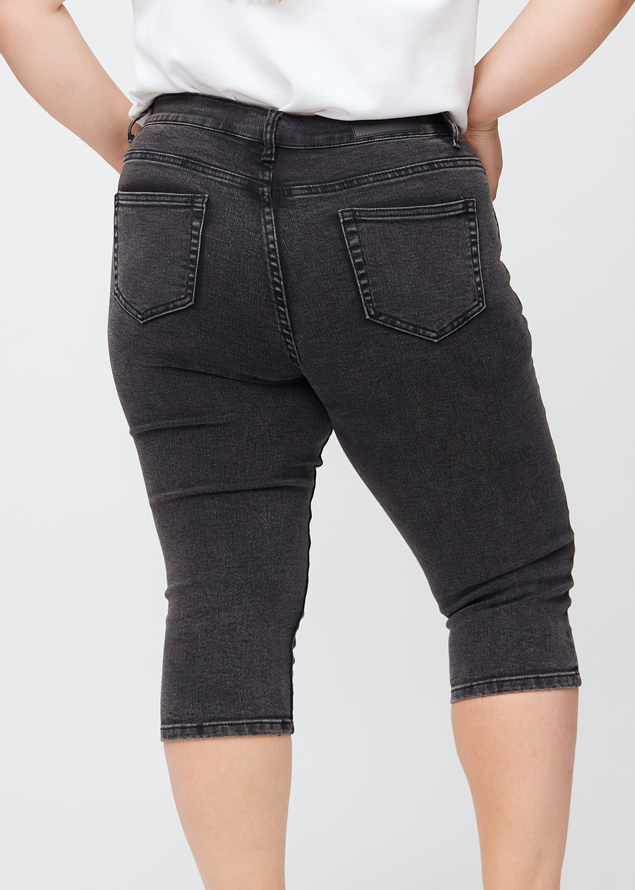 Skinny-capris til kvinner i mørkegrå denim, fargen Shadows. Nærbilde bakfra på en plus size-modell, med fokus på lommer og sømmer.