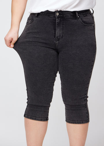 Skinny-capris til kvinner i mørkegrå denim, fargen Shadows. En plus size-modell strekker stoffet for å vise fleksibiliteten.