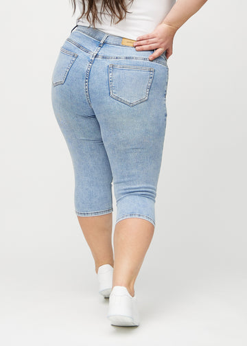Skinny-capris til kvinner i lyseblå denim, fargen Waves. Sett bakfra på en plus size-modell, med fokus på passform og baklommer.