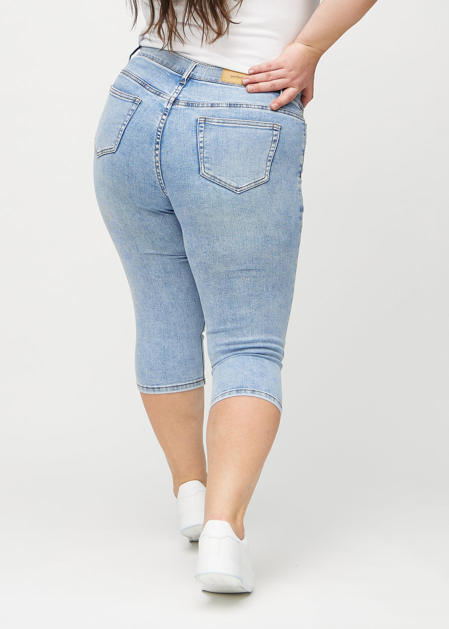 Skinny-capris til kvinner i lyseblå denim, fargen Waves. Sett bakfra på en plus size-modell, med fokus på passform og baklommer.