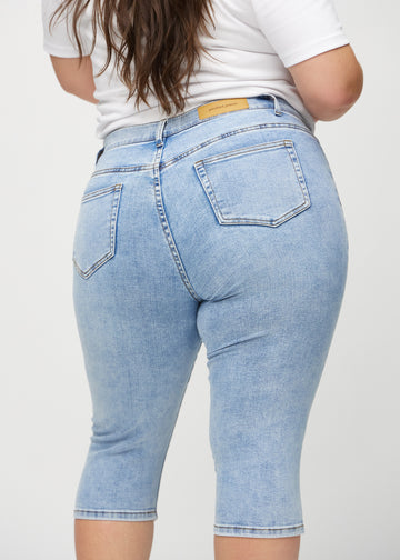 Skinny-capris til kvinner i lyseblå denim, fargen Waves. Nærbilde bakfra på en plus size-modell, med fokus på lommer og sømmer.