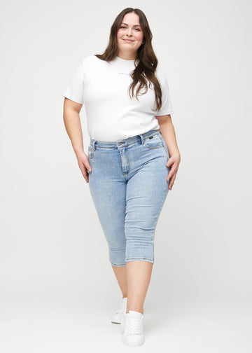 Skinny-capris til kvinner i lyseblå denim, fargen Waves. Helhetsbilde av en plus size-modell med capris på.