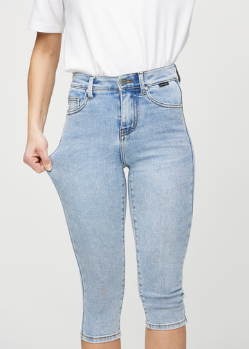 Skinny-capris til kvinner i lyseblå denim, fargen Waves. En modell strekker stoffet for å vise fleksibiliteten.