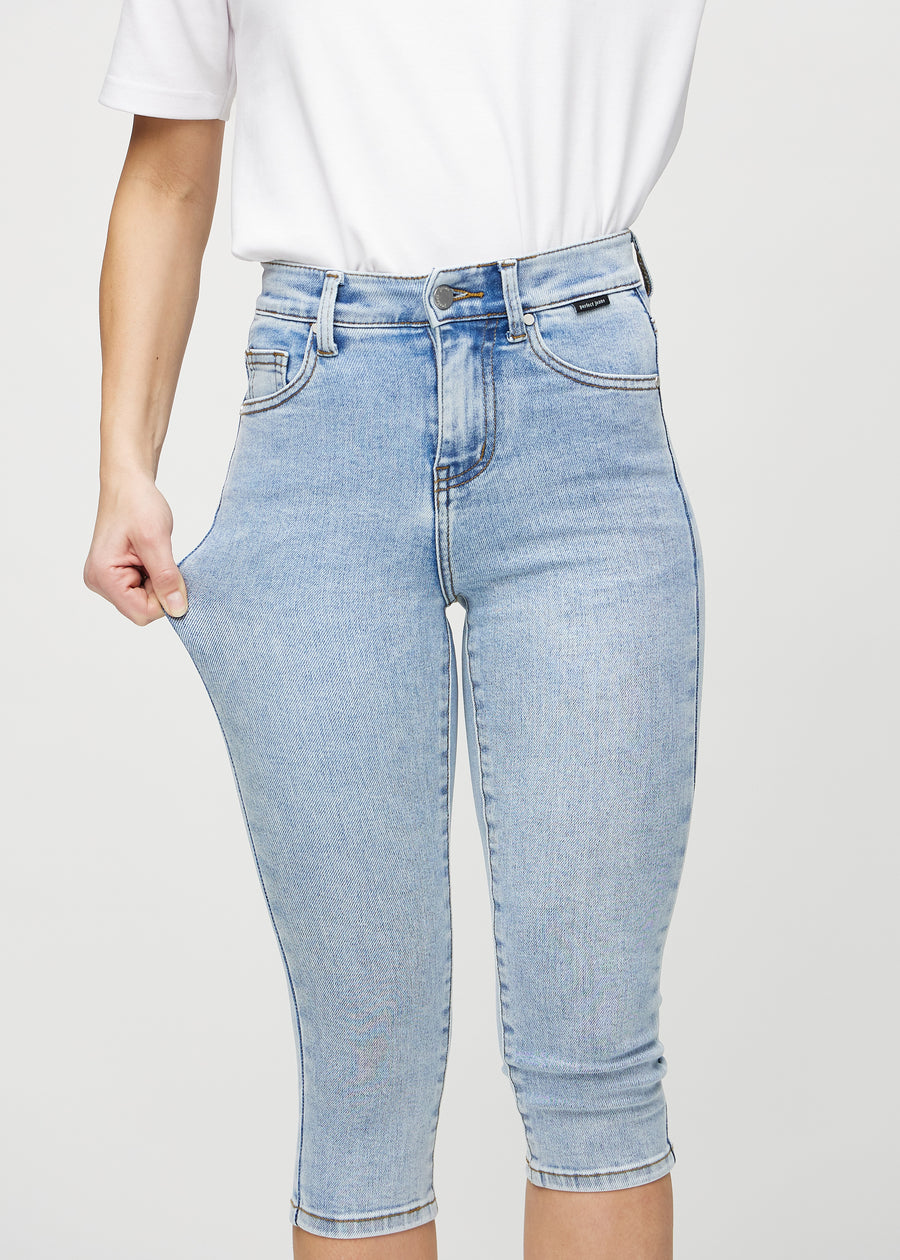 Skinny-capris til kvinner i lyseblå denim, fargen Waves. En modell strekker stoffet for å vise fleksibiliteten.