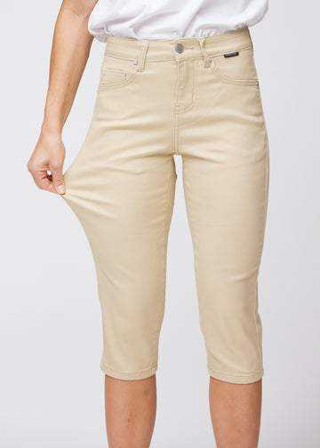 Slim-capris til kvinner i beige jeansstoff, fargen Gazelles. En modell strekker stoffet ved låret for å vise stretch og fleksibilitet.