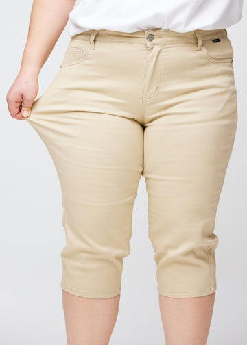 Slim-capris til kvinner i beige jeansstoff, fargen Gazelles. En plus size-modell strekker stoffet ved låret for å vise stretch og fleksibilitet.