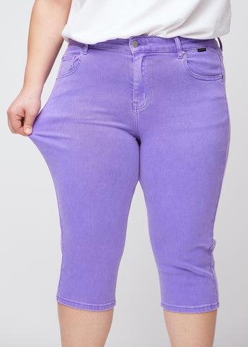 Slim-capris til kvinner i pastellilla jeansstoff, fargen Lavenders. En plus size-modell strekker stoffet ved låret for å vise stretch og fleksibilitet.