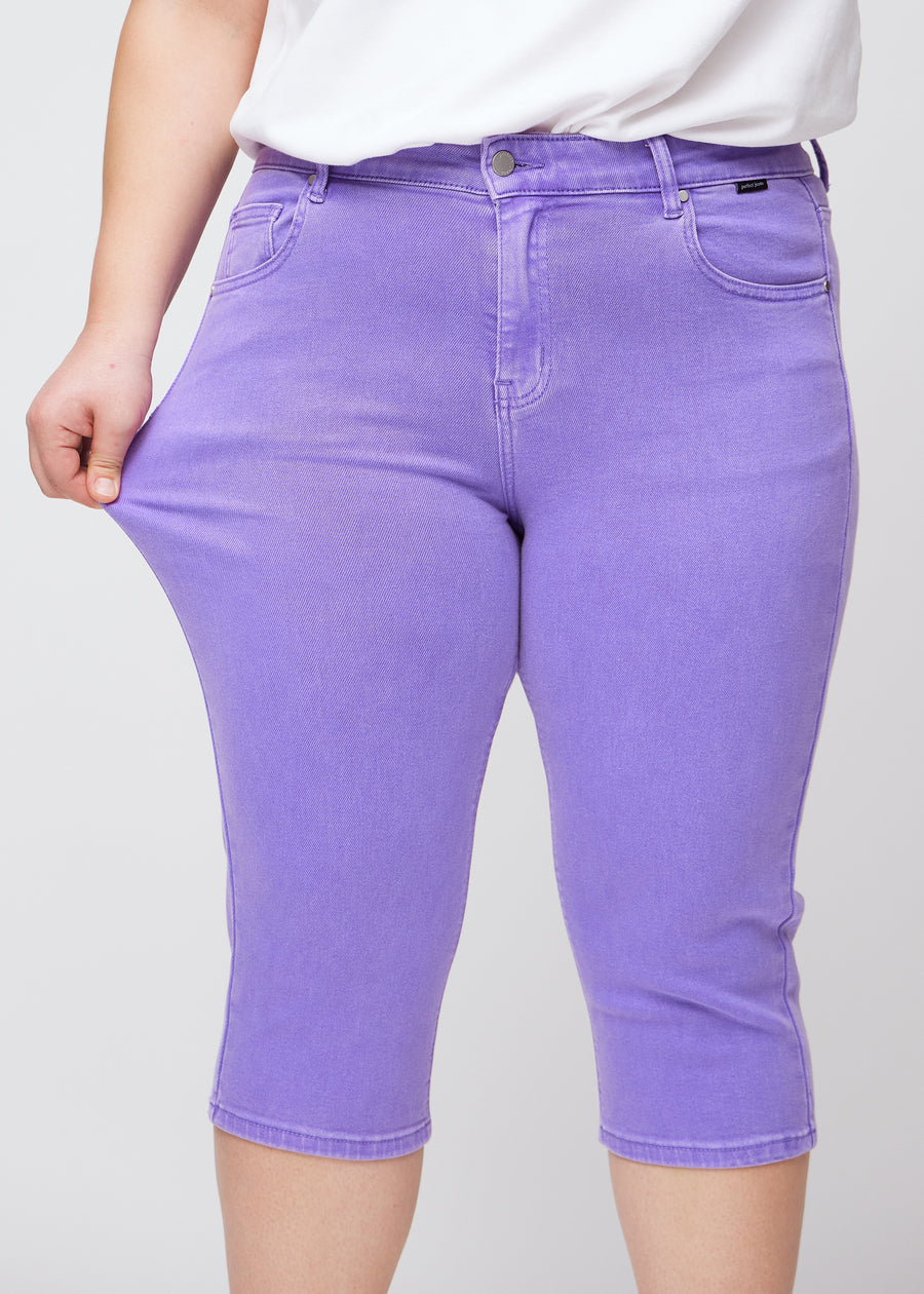 Slim-capris til kvinner i pastellilla jeansstoff, fargen Lavenders. En plus size-modell strekker stoffet ved låret for å vise stretch og fleksibilitet.