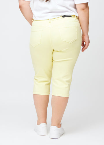 Slim-capris til kvinner i pastelllysegult jeansstoff, fargen Lemonades. Sett bakfra på en plus size-modell, med fokus på passform, lengde og baklommer.