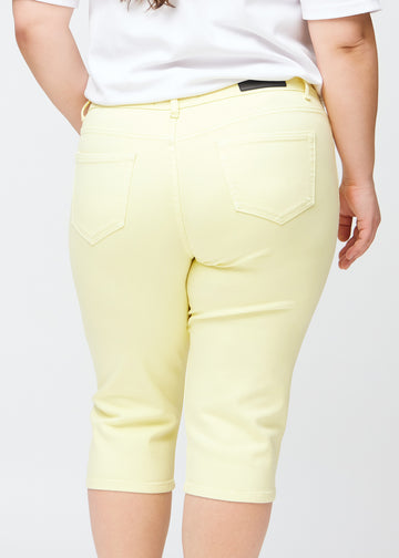 Slim-capris til kvinner i pastelllysegult jeansstoff, fargen Lemonades. Nærbilde bakfra på en plus size-modell, med fokus på baklommer og sømmer.