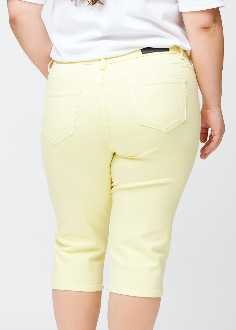 Slim-capris til kvinner i pastelllysegult jeansstoff, fargen Lemonades. Nærbilde bakfra på en plus size-modell, med fokus på baklommer og sømmer.