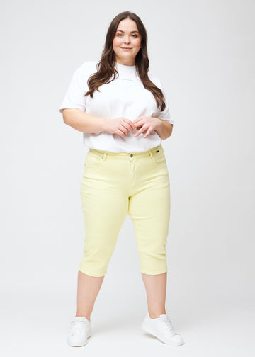 Slim-capris til kvinner i pastelllysegult jeansstoff, fargen Lemonades. Helhetsbilde av en plus size-modell med slim-capris.