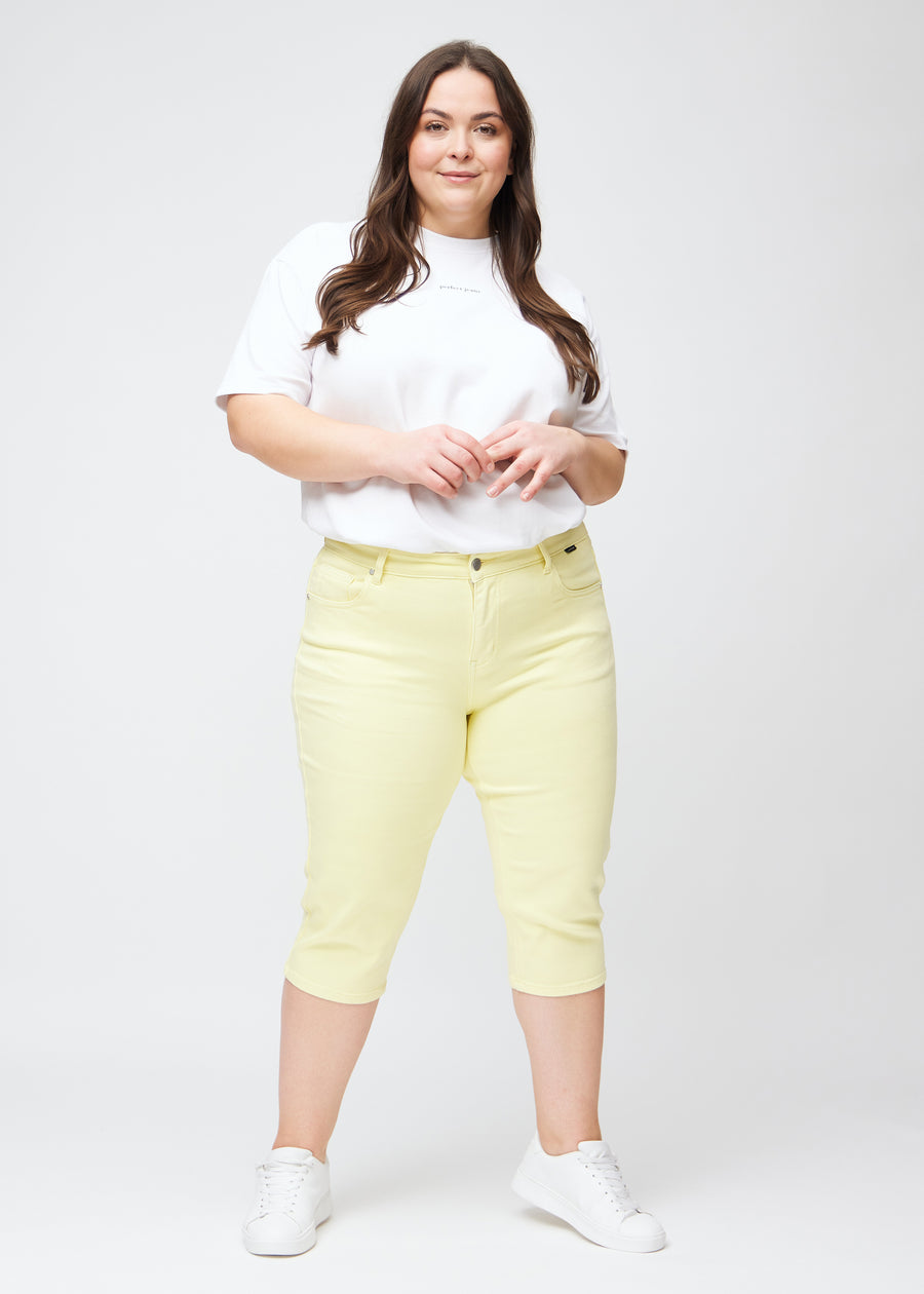 Slim-capris til kvinner i pastelllysegult jeansstoff, fargen Lemonades. Helhetsbilde av en plus size-modell med slim-capris.