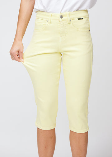 Slim-capris til kvinner i pastelllysegult jeansstoff, fargen Lemonades. En modell strekker stoffet ved låret for å vise stretch og fleksibilitet.