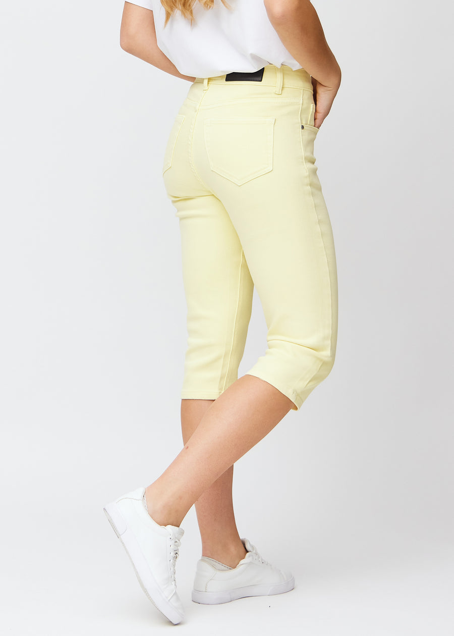 Slim-capris til kvinner i pastelllysegult jeansstoff, fargen Lemonades. Sett bakfra på en modell, med fokus på passform, lengde og baklommer.