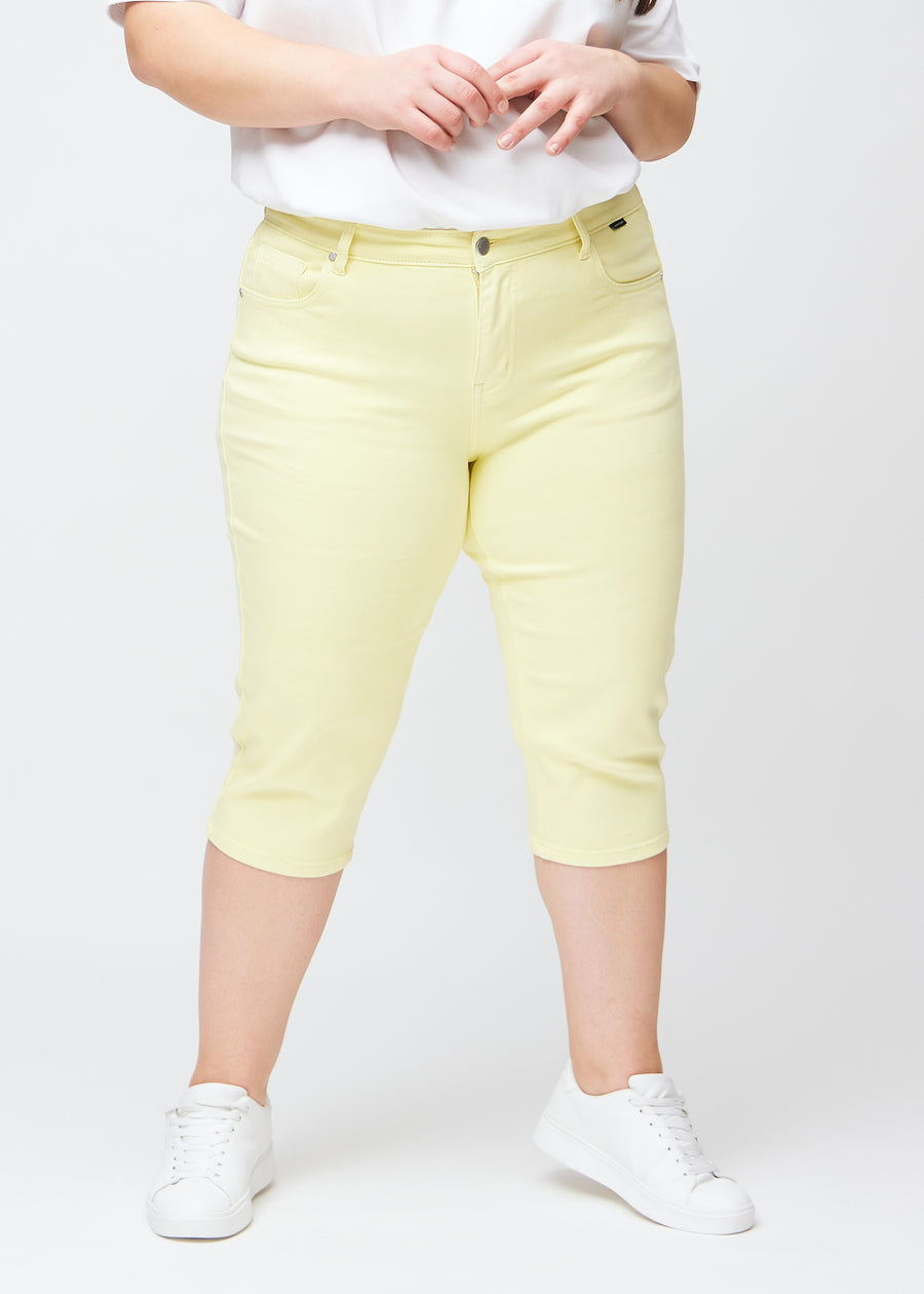 Slim-capris til kvinner i pastelllysegult jeansstoff, fargen Lemonades. Sett forfra på en plus size-modell, med figursydd passform til rett under kneet.