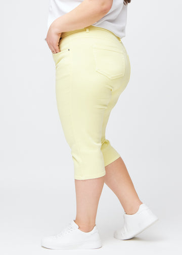 Slim-capris til kvinner i pastelllysegult jeansstoff, fargen Lemonades. Sett fra siden på en plus size-modell, med figursydd passform og mellomhøyt liv (Mid Rise).