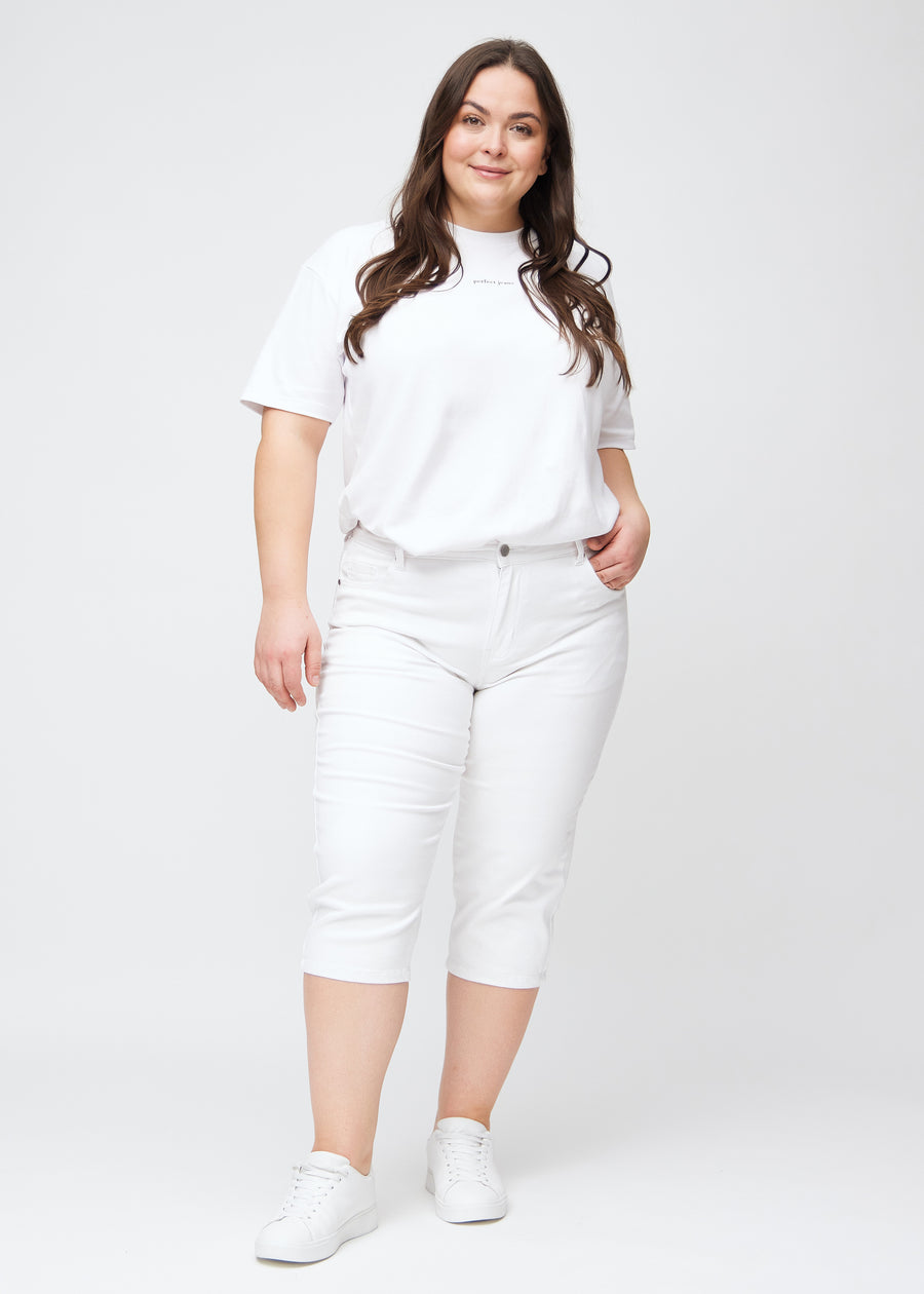 Slim-capris til kvinner i hvitt jeansstoff, fargen Marguerites. Helhetsbilde av en plus size-modell med slim-capris.