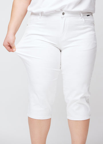 Slim-capris til kvinner i hvitt jeansstoff, fargen Marguerites. En plus size-modell strekker stoffet ved låret for å vise stretch og fleksibilitet.