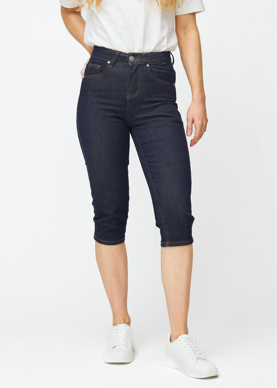 Dyp mørkeblå denim capris til dame i fargen Midnights med slim passform som er figursydd fra hoften til under kneet, sett forfra.